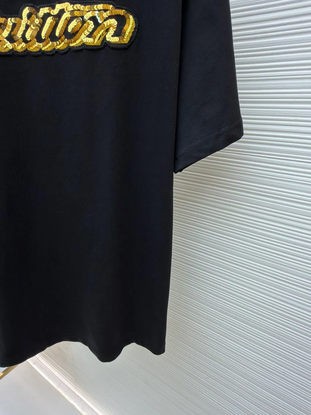 LOUIS VUITTON cotton round neck embroidered Vuitton signature logo short sleeves ●Original version: purchased and developed for 12300 ●Item number: 1682273-A10 ●Fabric: cotton fabric ●Technology: embroidery production ●Color: black ●Version: fitted version ●Weight: about 295 grams ●Size: S-M-L-XL ●Description: This white short-sleeved T-shirt is made of high-count combed cotton fabric and has been treated with pre-washing technology. It has a soft and skin-friendly touch and is not easy to deform. The silhouette of the shirt is a loose shoulder design, which meets the needs of modern casual wear. The core decoration area on the chest uses hand-beading and bronzing technology, and uses metallic gold sequins and embroidery threads intertwined to outline a three-dimensional letter pattern. The sequins are layered and inlaid, and each one is manually positioned and fixed by craftsmen to ensure a regular texture and uniform gloss. The edges of the letters are sewn with matte silk thread to form a visual contrast between gold and matte, while reinforcing the decorative structure to avoid falling off during wear. The neckline uses double-needle hemming technology and is matched with ribbed cuffs of the same fabric. It is durable and fits the neck. The overall craftsmanship combines handicraftsmanship with modern clothing technology, and the details show exquisite texture. The overall wiring is straight and delicate, the fabric is comfortable and soft, and the color is consistent without color difference. It can be matched with the same style to create a fashionable look and control various occasions. Customized accessories, complete with three standards, same style for men and women!